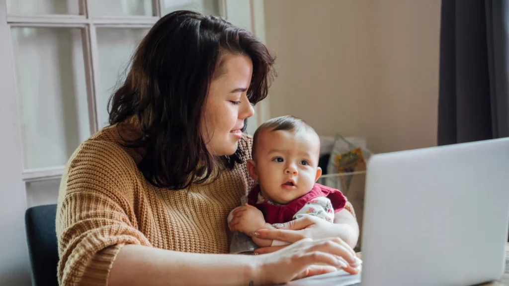 Woman using a computer whilst holding a baby