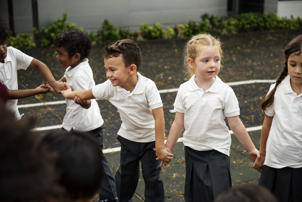 Group of diverse primary school students standing holding hands in playground